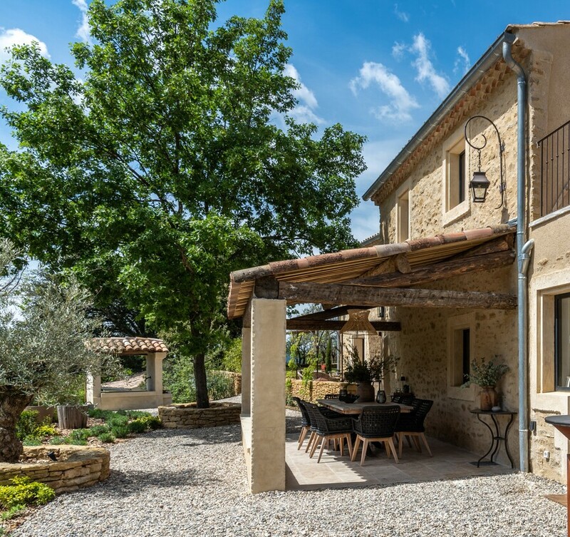 Maison en pierre provençale avec terrasse couverte et salle à manger extérieure. Grand jardin méditerranéen en gravier.